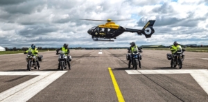 Four motorcycle riders at Cardiff airport on the runway with a helicopter behind them